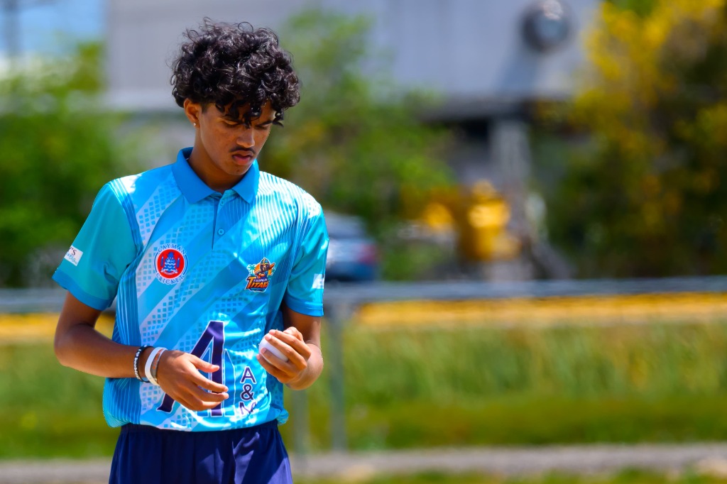 Close-up of young bowler holding white cricket ball examining seam