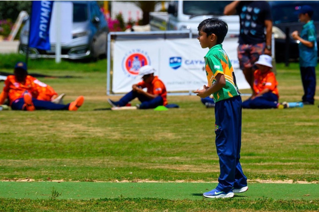 Junior cricketer in green and gold jersey alert on the pitch